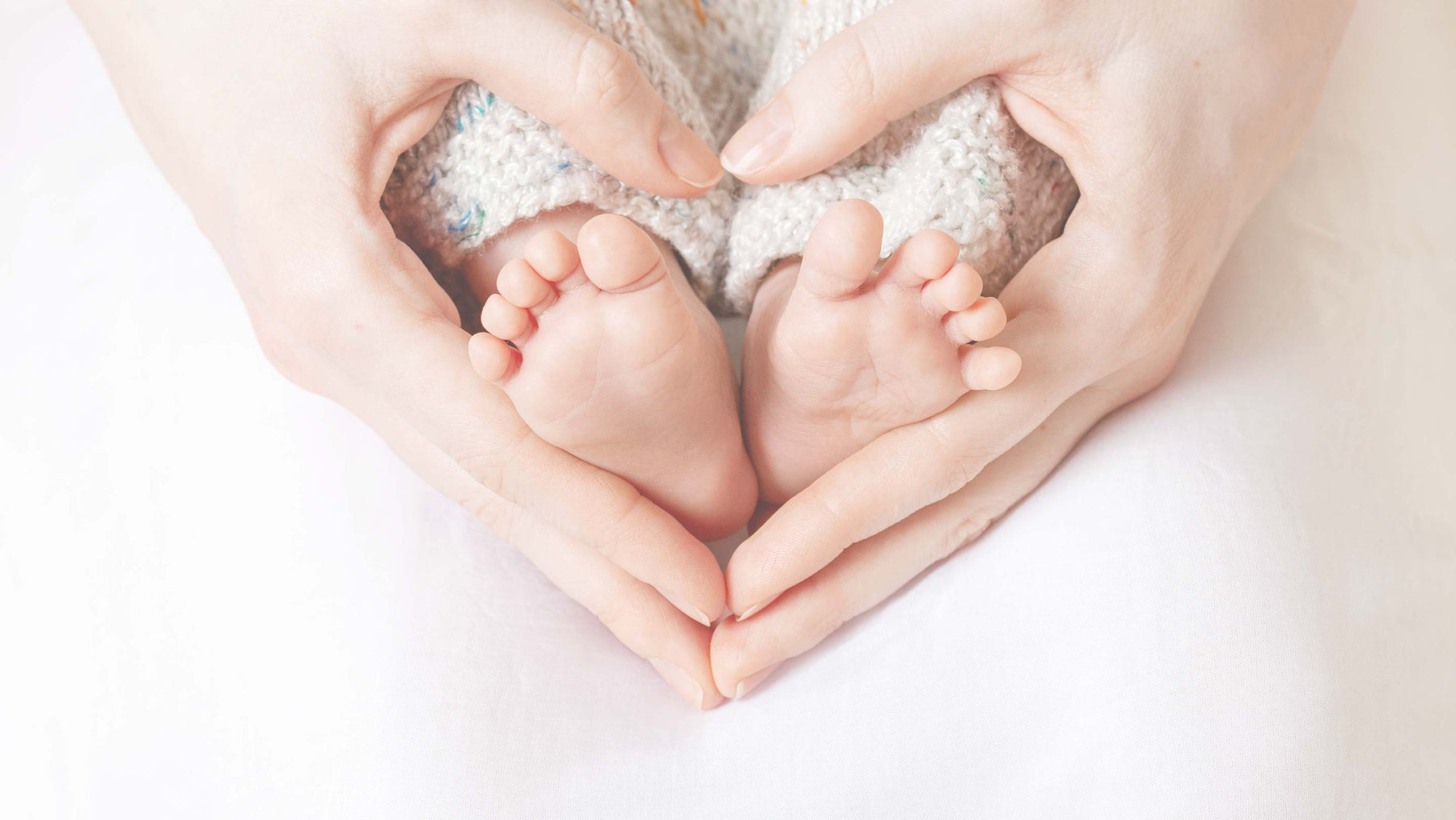 A woman's hands cupping a baby's feet in a heart shape